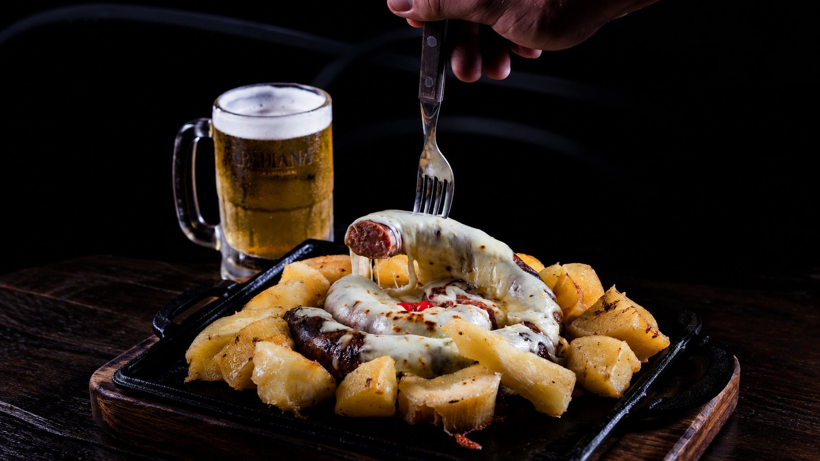 Linguiça recheada com queijo gratinado e mandioca na chapa, servida com chopp